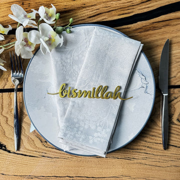 Altın Bismillah yazılı peçete süsü, beyaz peçeteli tabakta orkide yanında sofra düzeni