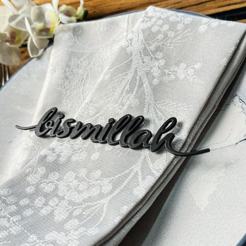 Siyah Bismillah yazılı metal peçete süsü, beyaz desenli peçetenin üstünde yakın çekim