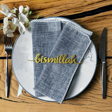 Altın Bismillah yazılı metal peçete süsü, mavi keten peçetenin üstünde tabakta