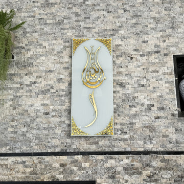 Beyaz cam üzerine altın akrilik hatlı lale formlu Maşallah hatlı temperli cam tablo, taş duvarda yakın görünüm