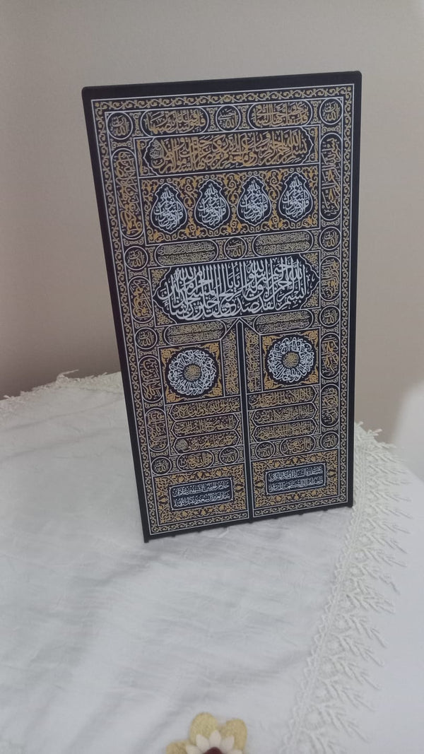 Kutsal mekânlar: beyaz örtü üzerinde duran Kâbe kapısı motifli tablo