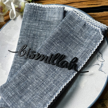 Siyah Bismillah yazılı metal peçete süsü, mavi keten peçetenin üstünde yakın çekim