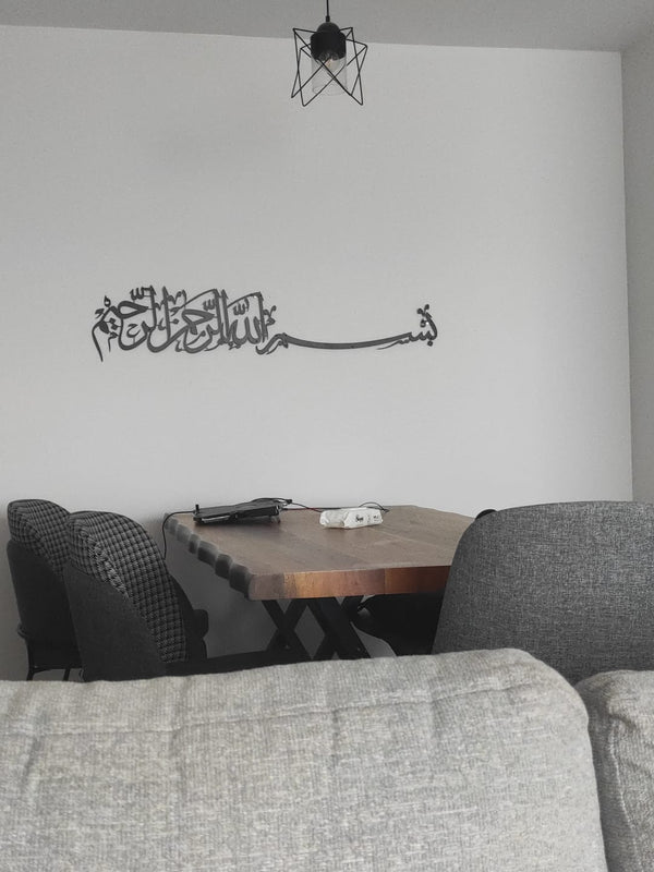 Yemek masası olan odada duvarda gri Besmele hattı