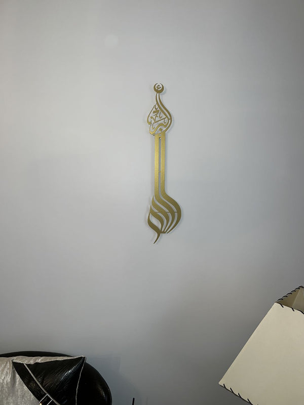Duvarda altın renkli dikey Allah lafzı, minare biçimli hat