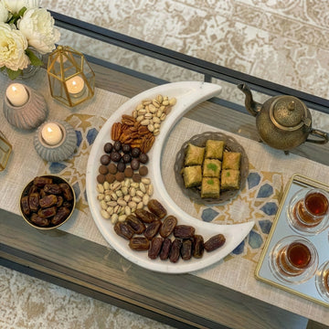 Hilal mermer servis tabağında hurma ve kuruyemişler, çay bardaklı iftar masasında üstten