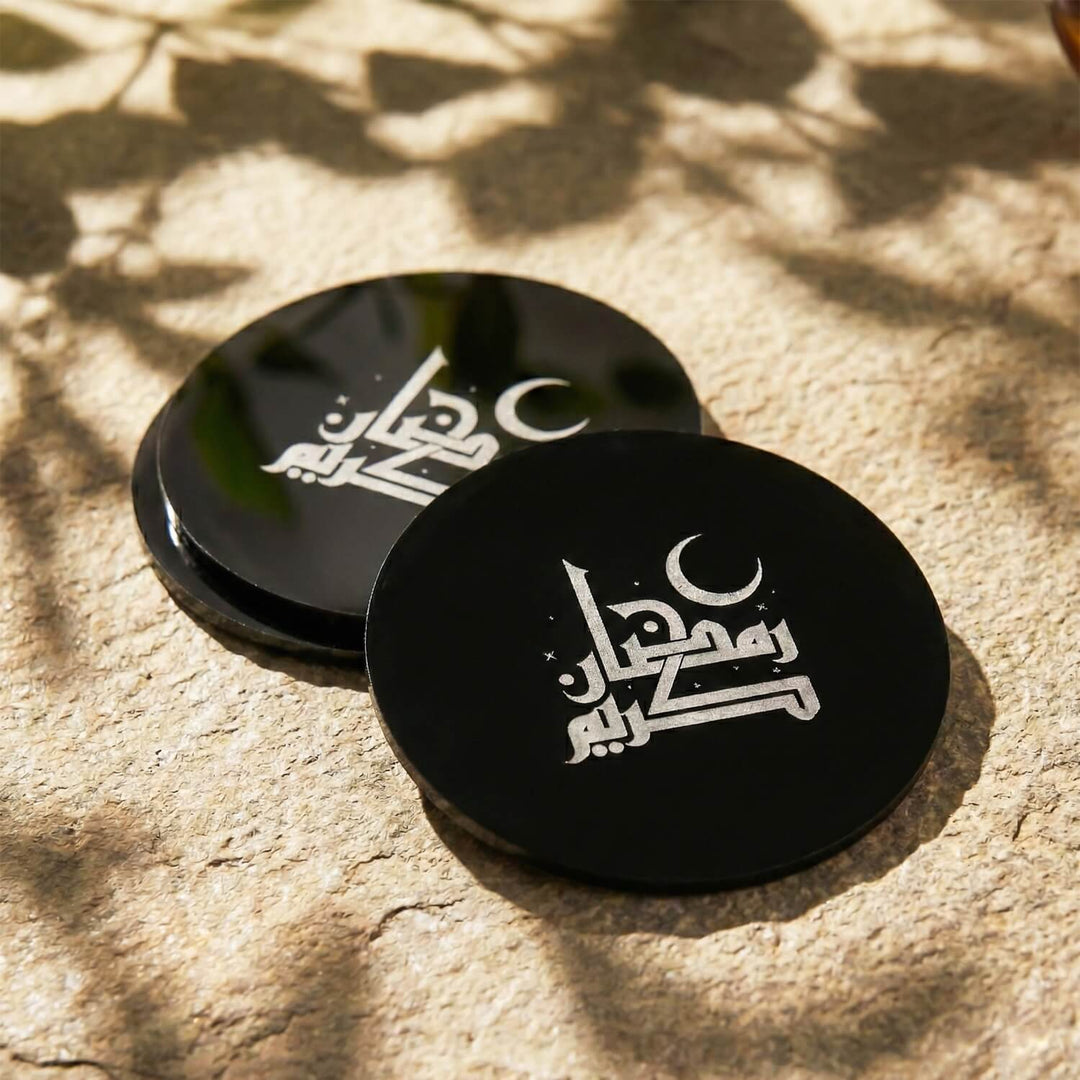 Fatimi Kufi Hat Ramazan Kerim yazılı iki siyah akrilik bardak altlığı, yan yana ve üst üste