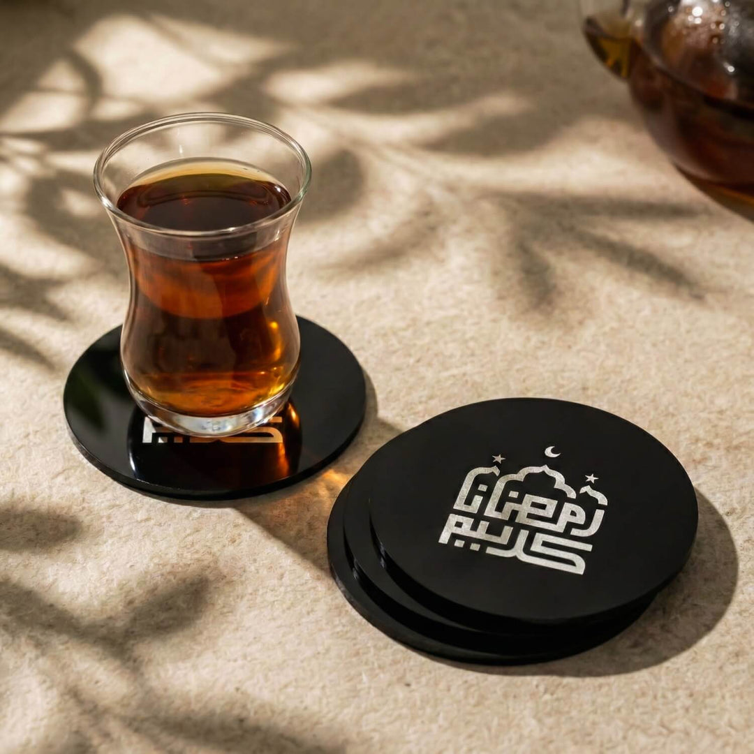 Kufi Hat Ramazan Kerim yazılı siyah akrilik bardak altlığı, üzerinde çay bardağı