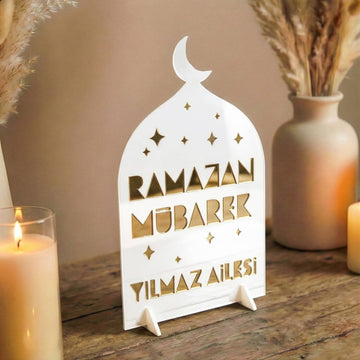 Aile İsimli Geometrik akrilik Ramazan masa üstü dekor, dış beyaz iç altın, ahşap masada mum ve vazo yanında, Türkçe yazılı