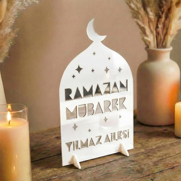 Aile İsimli Geometrik akrilik Ramazan masa üstü dekor, dış beyaz iç gümüş, ahşap masada mum ve vazo yanında, Türkçe yazılı