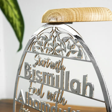 Parlak Gümüş metal mumluğun Bismillah yazısı ve ahşap tabla detayının yakın çekimi