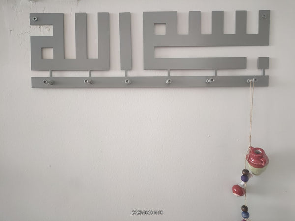 Duvarda gri Besmele yazılı kufi anahtarlık, askılarında takılar
