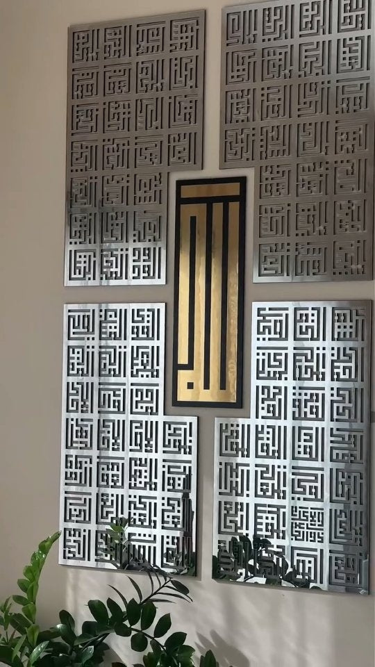 Duvarda gümüş ve altın renkli dört parçalı kufi hat tablosu, yanında bitkiler