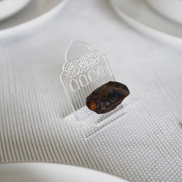 Şeffaf besmele yazılı kubbe şekilli akrilik hurmalık, beyaz sofra örtüsünde hurma ile