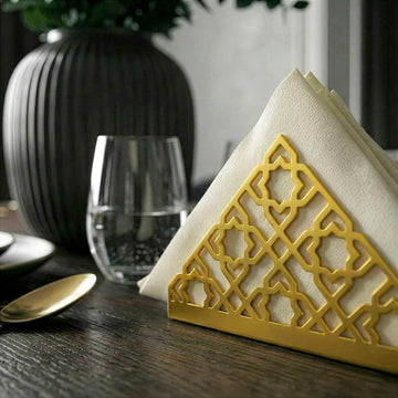 Geometrik desenli altın metal peçetelik, koyu ahşap yemek masasında bardak yanında yakın kadraj