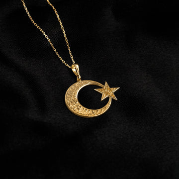 Altın kaplama ay yıldız kolye, sol üstten inen ince zincirle siyah kumaş üzerinde küçük kolye ucu
