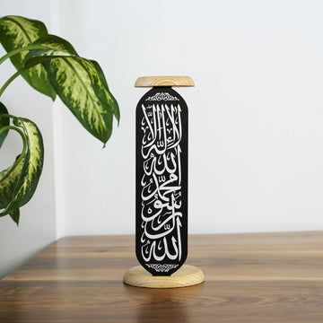 Siyah metal Kelime-i Tevhid mumluğu, beyaz Arapça yazı ve ahşap üst tabla, ahşap masanın üstünde