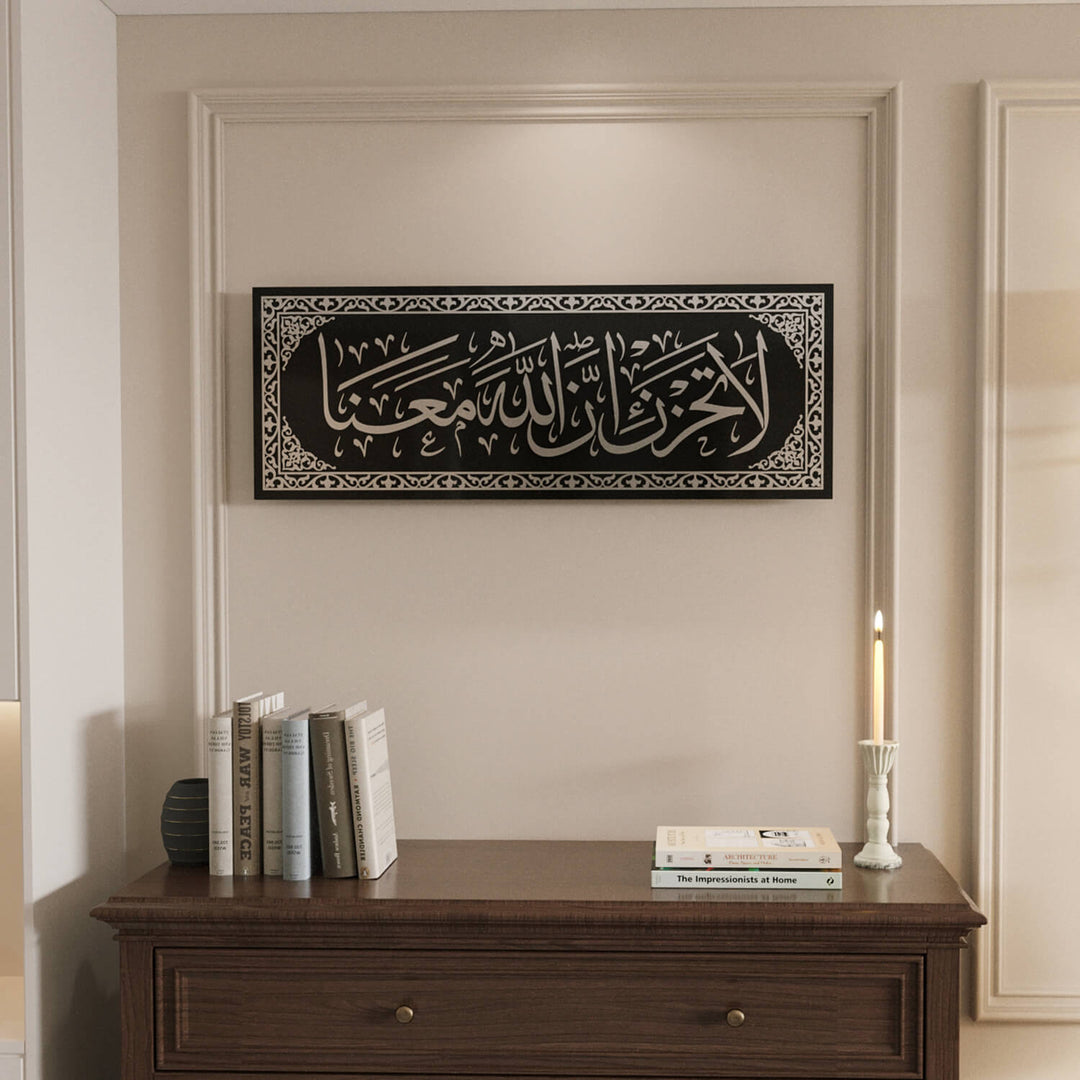 Geometrik çerçeve desenleri ile detaylandırılmış zarif La Tahzen İnnallahe Meana Cam Tablo - Tevbe Suresi 40. Ayet.