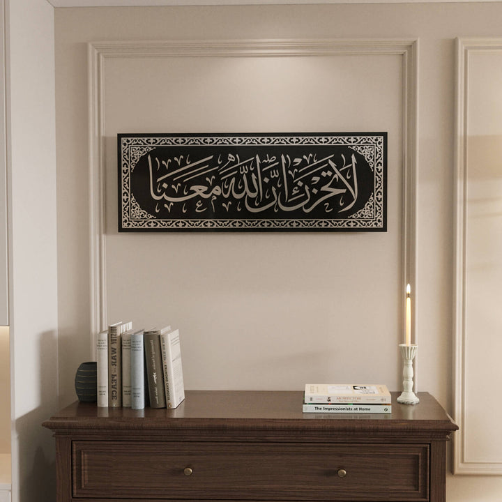 Geometrik çerçeve desenleri ile detaylandırılmış zarif La Tahzen İnnallahe Meana Cam Tablo - Tevbe Suresi 40. Ayet.