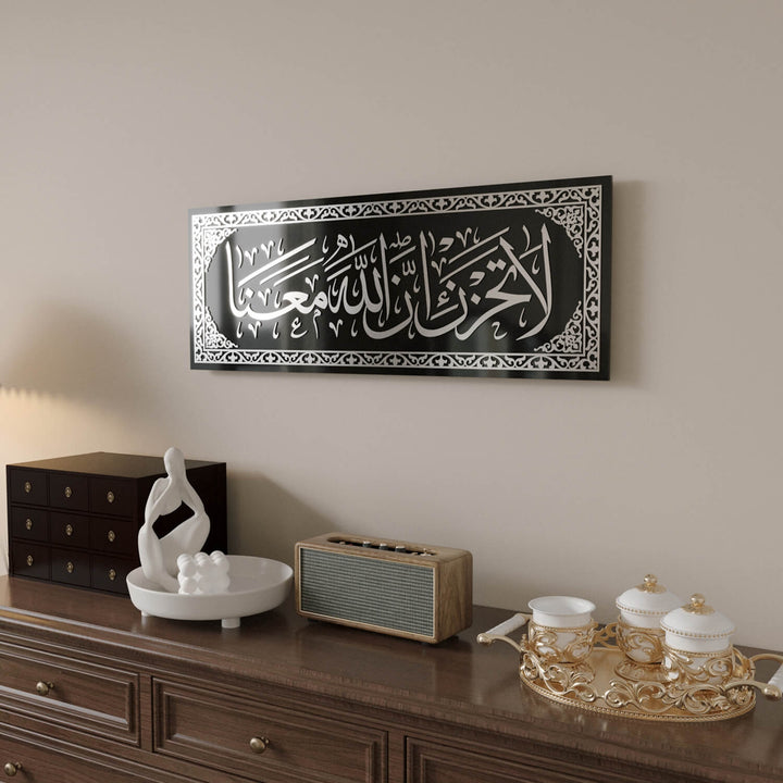 Minimalist ve klasik iç mekan tasarımlarına uyum sağlayan La Tahzen İnnallahe Meana Cam Tablo - Tevbe Suresi 40. Ayet.