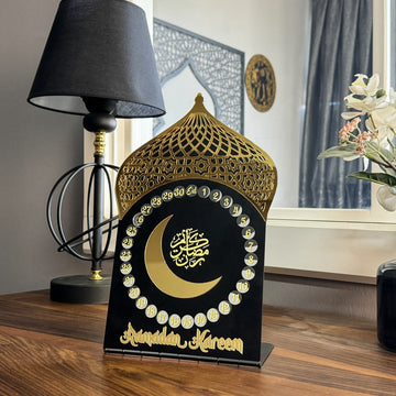 Mihrap formlu siyah metal Ramazan takvimi, altın akrilik hilal ve kubbe süslemeli, lambanın yanında