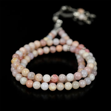 Pembe opal 99'luk tesbih, 6 mm doğal taş habbeler ve metal püskül, siyah fonda yakın çekim
