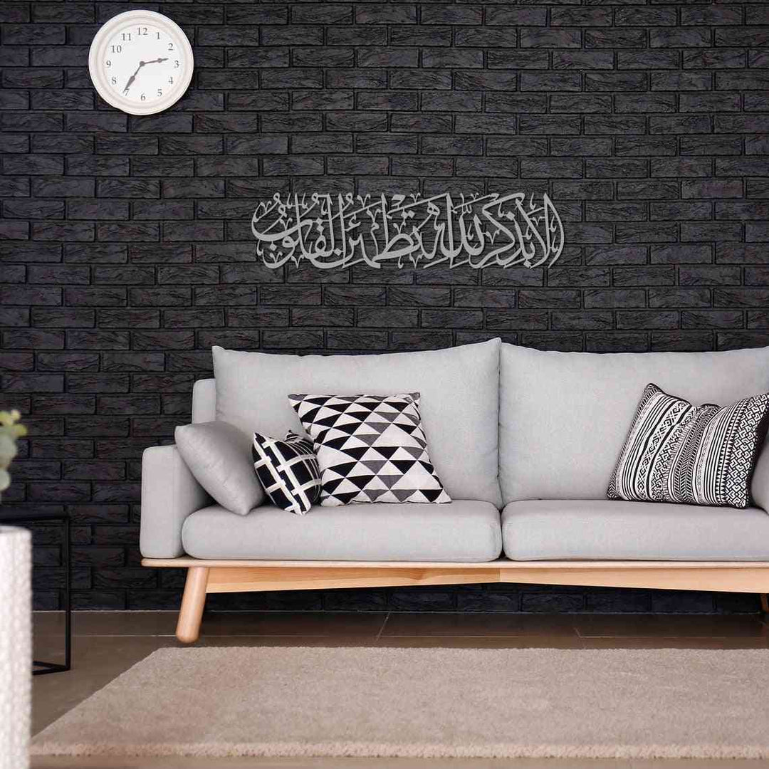 Rad Suresi 28. Ayet gümüş metal tablo, koyu tuğla duvarda gri koltuğun üzerinde