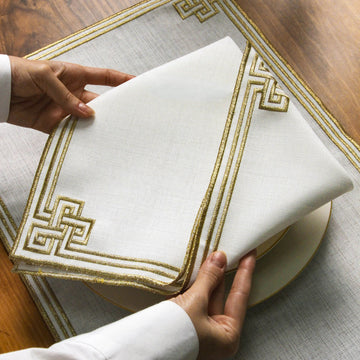 Altın nakışlı beyaz peçetenin katlanmış köşesi ve geometrik motifi, tabağın üstünde