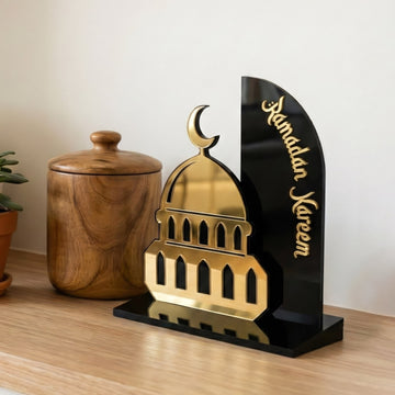 Altın cami silüetli ve siyah arka panelli akrilik Ramazan Kerim dekoru, ahşap kavanozun önünde