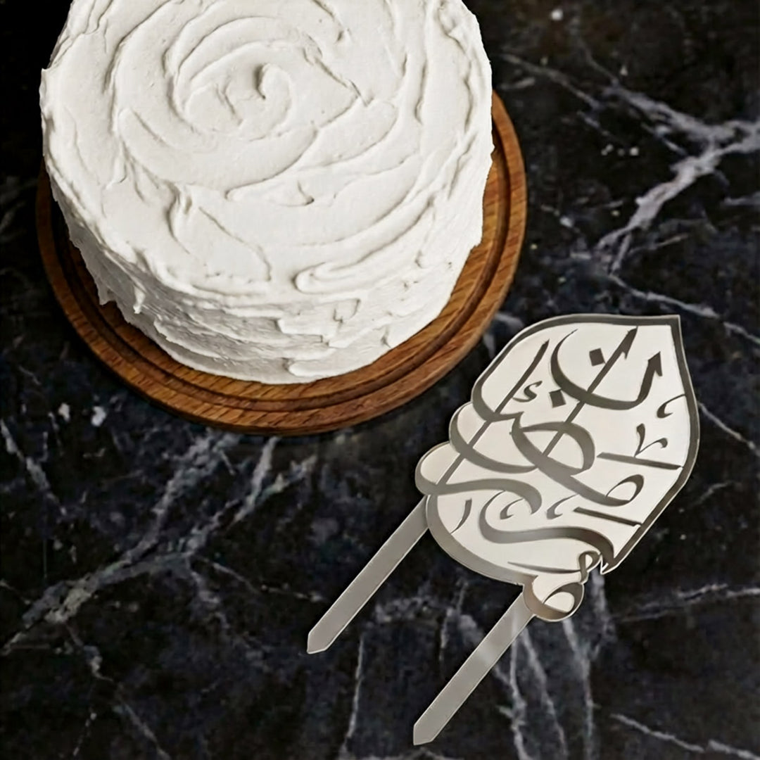 beyaz kremali pastanin ustten gorunumu ve yaninda yerlestirilmis gumus renkli arapca ramazan kerim yazili buzlu beyaz akrilik kek topper islamicwallarttr