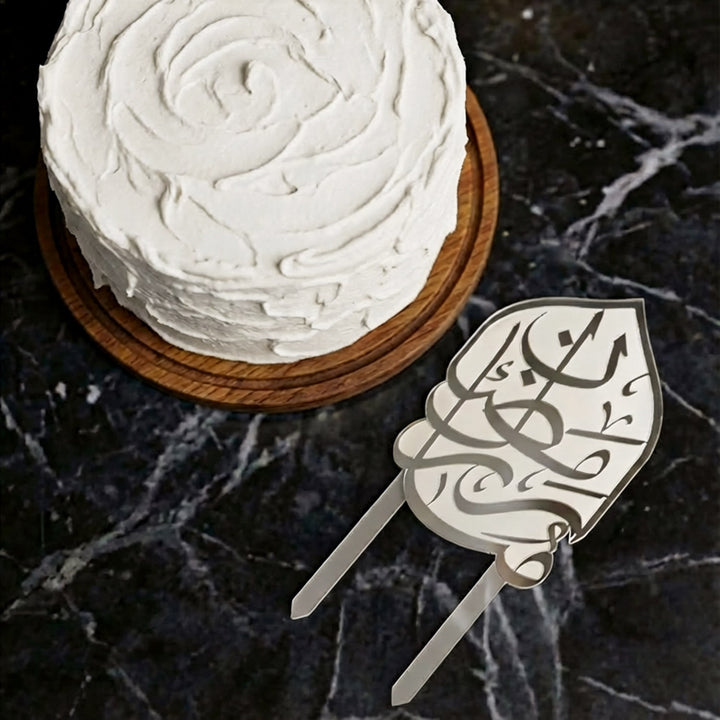 beyaz kremali pastanin ustten gorunumu ve yaninda yerlestirilmis gumus renkli arapca ramazan kerim yazili buzlu beyaz akrilik kek topper islamicwallarttr