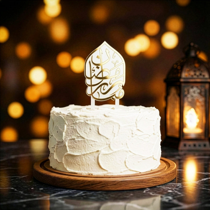 beyaz kremayla kapli yuvarlak pastanin uzerinde altin renkli arapca ramazan kerim yazili beyaz akrilik kek topper arka planda los isiklar ve dekoratif fener ile sik ramazan sunumu islamicwallarttr