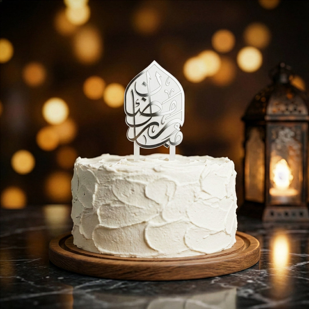 beyaz kremayla kapli yuvarlak pastanin uzerinde gumus renkli arapca ramazan kerim yazili beyaz akrilik kek topper arka planda los isiklar ve dekoratif fener ile sik ramazan sunumu islamicwallarttr