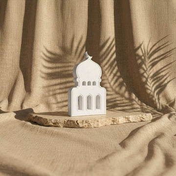 Taş cami biblo, üç kemerli pencereleri ve hilalli kubbesiyle bej fonda karşıdan görünüm