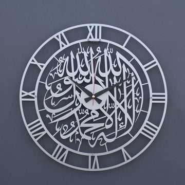 Gümüş Romen rakamlı Kelime-i Tevhid metal duvar saati, gri duvarda ön görünüm