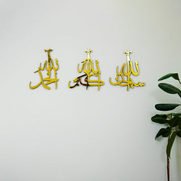 Altın renk Sübhanallah, Elhamdülillah, Allahuekber üç ayrı parçalı akrilik set, beyaz duvarda bitki yanında